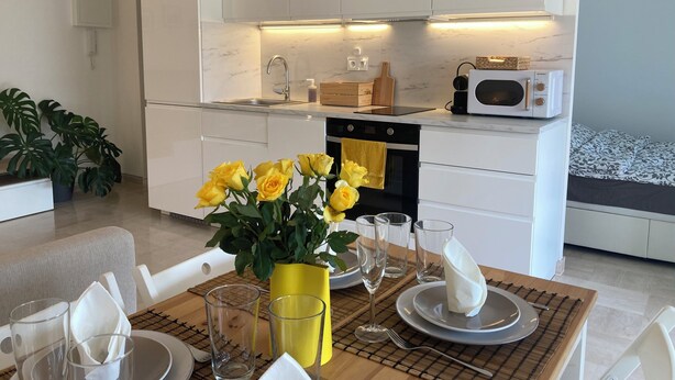 Une cuisine moderne avec des meubles blancs, un four à micro-ondes et un évier. On y trouve une table à manger ornée d’un vase rempli de fleurs jaunes et d’un set de table.
