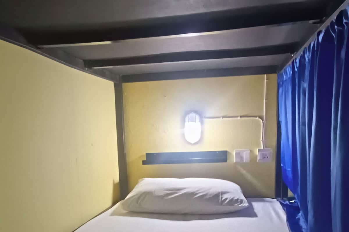A bunk bed with a single bed at the top and a lower bunk. There is a window with a view of the outside, a small shelf above the bed, and a power outlet on the wall.