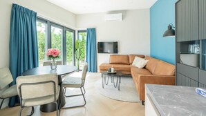 A modern living room with a sofa, TV, dining table, chairs, and a large window with curtains. - Welcome to Muralt 110, a modern chalet with everything for a carefree stay. Enjoy the cozy living ro (Scharendijke)