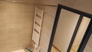 Een moderne badkamer met beige tegels, een houten vloer, een handdoekrek en een douchehoek.