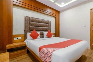 Una habitación de hotel con una cama grande, cabecera de madera y colcha estampada en rojo y blanco.