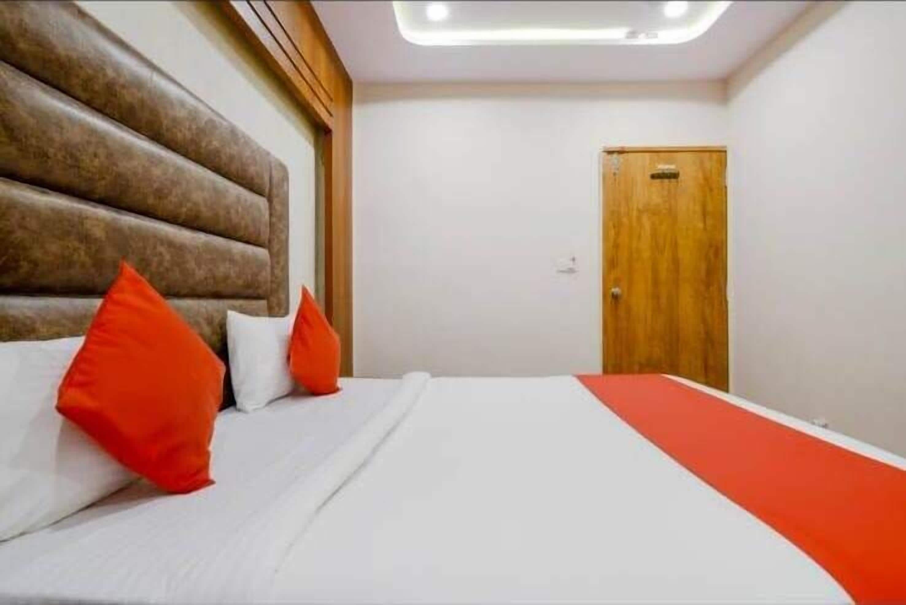 A hotel room with a wooden headboard, a bed with white bedding and red accents, and a wooden door.