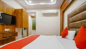 A hotel room with a bed, a TV mounted on the wall, and an air conditioning unit.