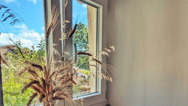 Een kamer met een raam, een vaas met gedroogde planten en een betegelde bank.