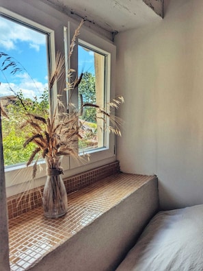 Et værelse med et vindue, en vase med tørrede planter og en flisebelagt bænk.