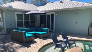 Un espace aménagé au bord de la piscine, avec une piscine à eau claire, un grand canapé d’angle, deux fauteuils Adirondack et une pergola dotée d’un parasol.