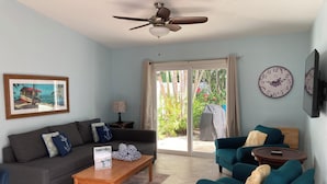 Un salon comprenant un canapé, une table basse et deux fauteuils. On y trouve également un ventilateur de plafond, une horloge et un tableau encadré accroché au mur.