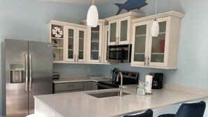 Une cuisine moderne avec des meubles blancs, des appareils en acier inoxydable, un îlot central doté de tabourets et un poisson décoratif accroché au mur.
