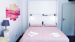 Ein Hotelzimmer mit Bett, Fernseher, Schreibtisch und einer Wand mit einem Gemälde von einem rosafarbenen Sonnenuntergang.