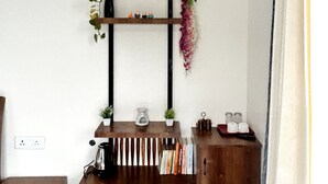 Une étagère en bois, ornée de plantes et de livres, un radiateur et une prise électrique sur un mur blanc.