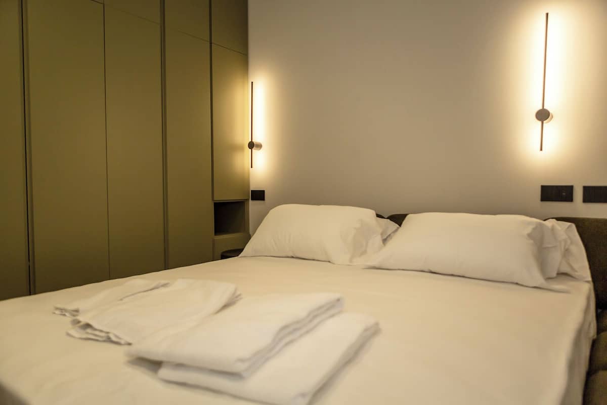 A hotel room with a neatly made bed, a wardrobe, and two wall-mounted light fixtures.