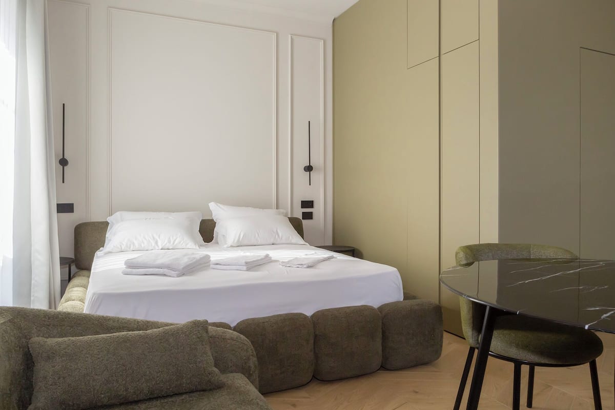 A modern hotel room with a neatly made bed, a dining table, and a sofa.