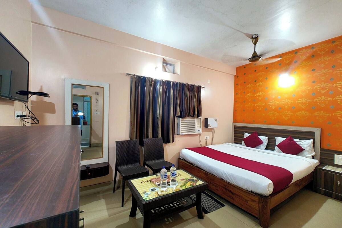 Habitación de hotel con cama, escritorio, dos sillas, una mesita de centro, unidad de aire acondicionado y ventilador de techo.
