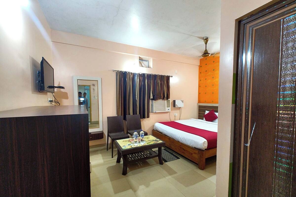 Habitación de hotel con cama, escritorio, silla, televisor y ventana con cortinas.