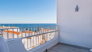 A balcony with white chairs and a table, overlooking a beach with orange buildings and the sea. - Apartment Atlas (Albufeira)