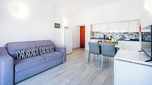 A modern kitchen with white cabinets, a dining area with a table and chairs, and a living area with a sofa and a TV. - Apartment Atlas (Albufeira)