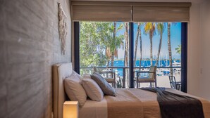 A bedroom with a large bed, a view of the beach, and a balcony with chairs and tables. - 5-Minute Walk to the Malecón — Your Baja Oasis with Sun, Pool & Space to Unwind (La Paz)
