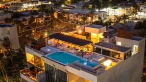 A modern multi-story building with a rooftop pool area, multiple balconies, and a view of the cityscape at night. - 5-Minute Walk to the Malecón — Your Baja Oasis with Sun, Pool & Space to Unwind (La Paz)