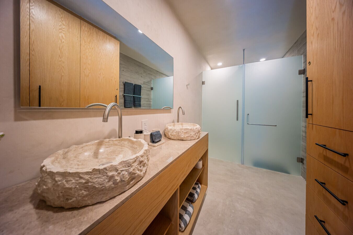 A modern bathroom with two large stone sinks, a wooden vanity, and a large mirror.