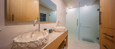 A modern bathroom with two large stone sinks, a wooden vanity, and a large mirror.