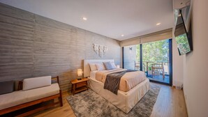 A modern bedroom with a large bed, a sofa, a small table with a lamp, and a view of the outdoors through a sliding glass door. - 5-Minute Walk to the Malecón — Your Baja Oasis with Sun, Pool & Space to Unwind (La Paz)