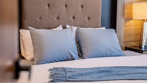 Una cama bien hecha con tablero tapizado, dos almohadas y una manta azul.