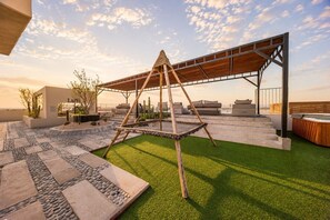 A rooftop terrace with a swing set, outdoor seating, and a view of the horizon.