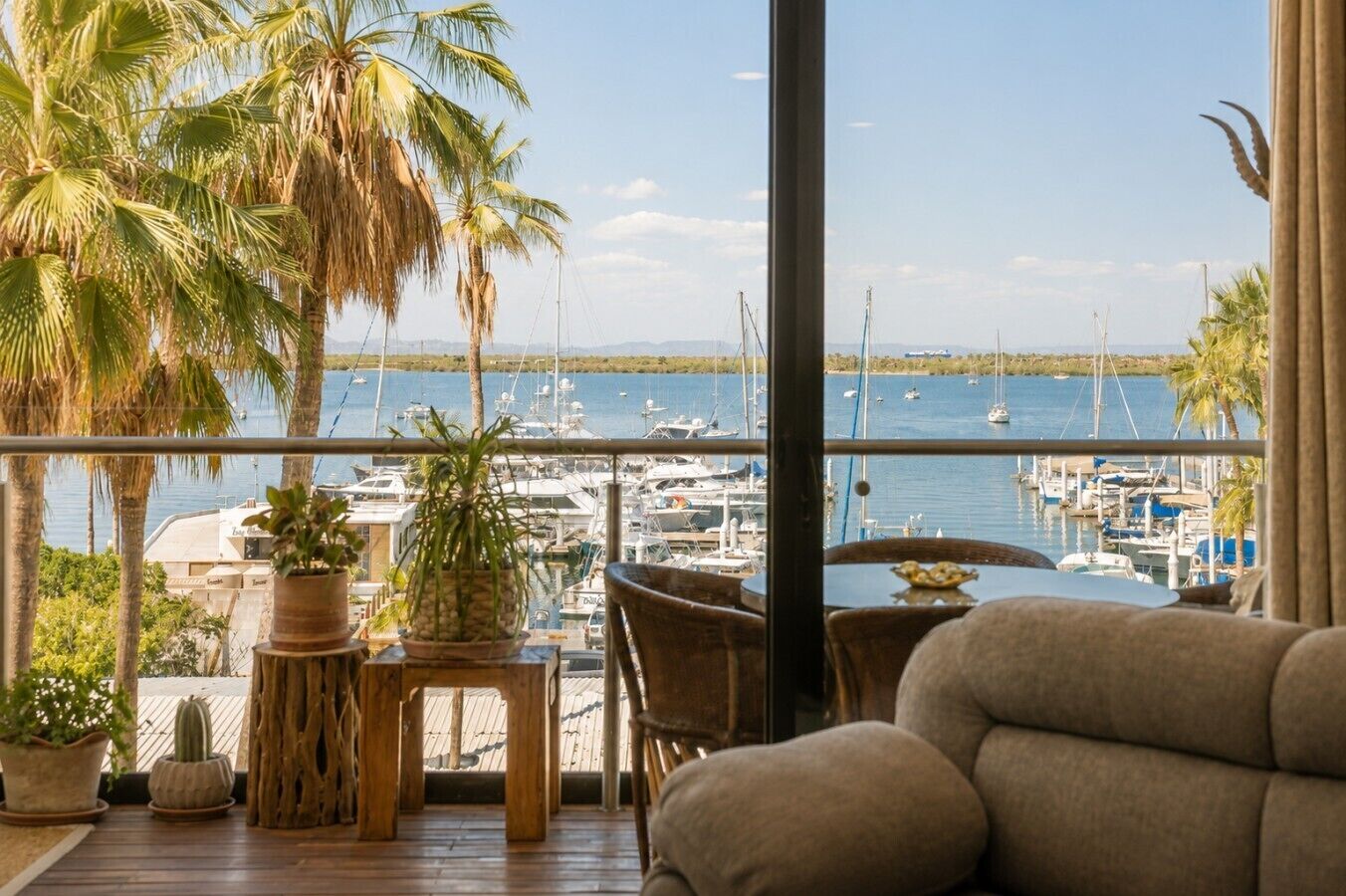 A balcony with a view of a marina, wooden furniture, and potted plants.