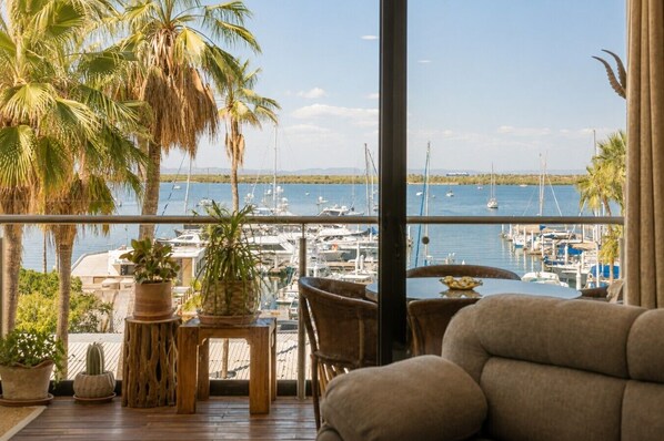 A balcony with a view of a marina, wooden furniture, and potted plants.