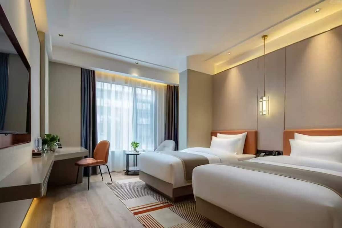 Habitación de hotel con dos camas, un escritorio, una silla y un televisor.