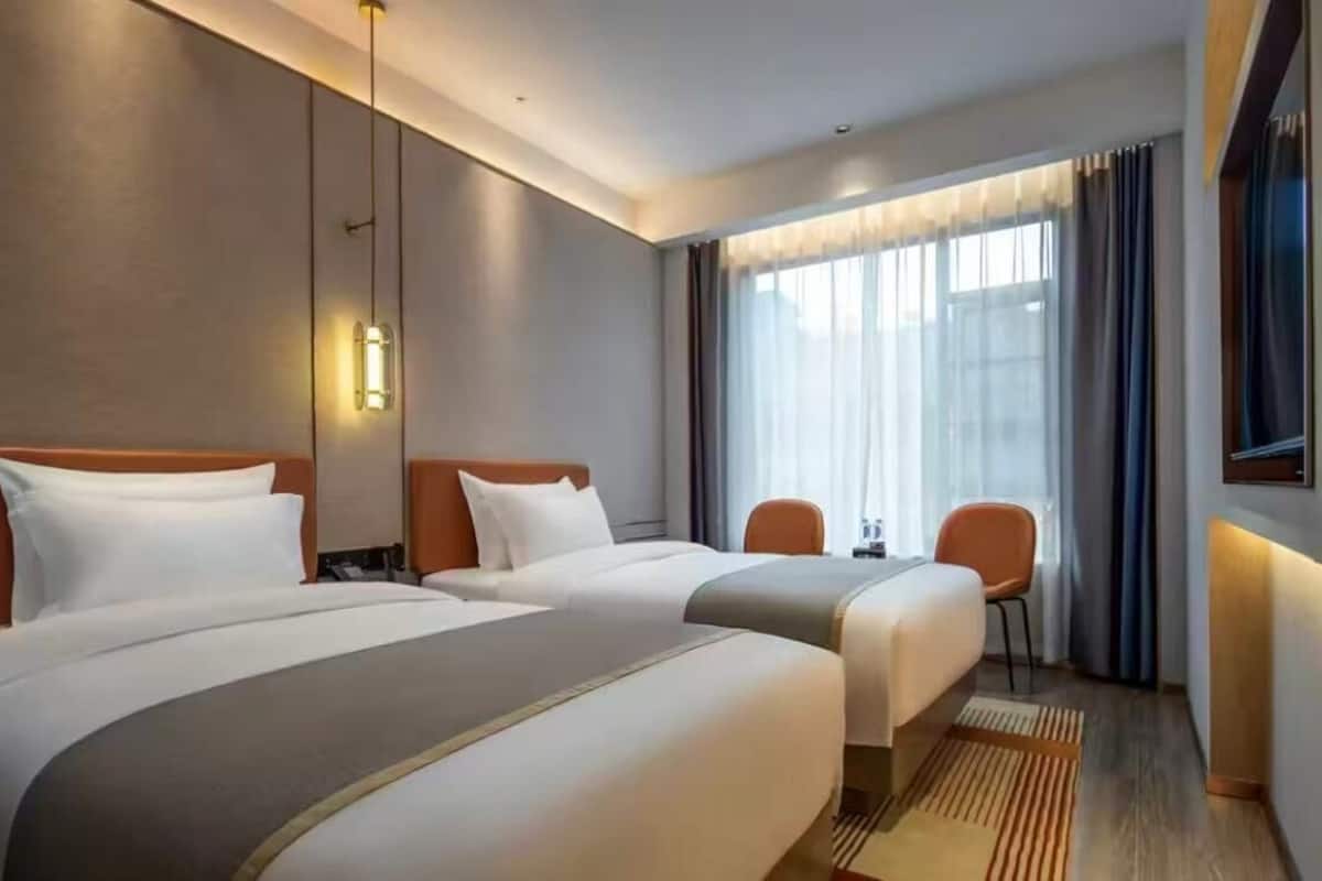 Habitación de hotel con dos camas, un escritorio, sillas y un ventanal grande con cortinas.