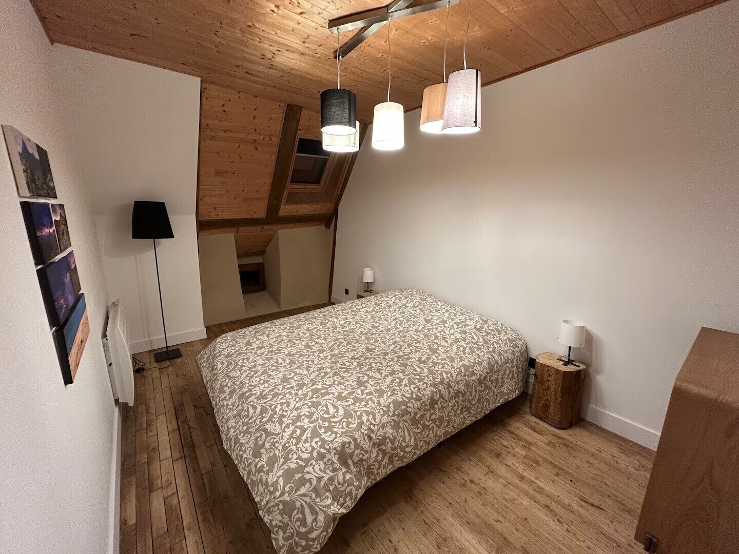 Een slaapkamer met een houten plafond, een bed met een geborduurde spreidek en een vloerlamp, plus een klein nachtkastje met een lamp.