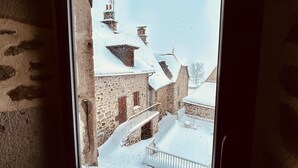 Ein Fenster mit Blick auf einen verschneiten Innenhof mit Steingebäuden und einem Metallgeländer.