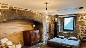 Ein gemütliches Zimmer mit Steinwand, Holzboden, einem Bett, einem Stuhl und einer kleinen Kommode.