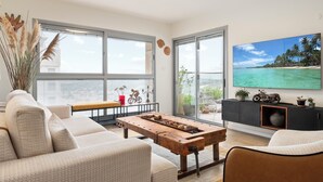 A modern living room with a large window, a wooden coffee table, a sofa, and a television displaying a tropical beach scene. - Poleg Beach Seaview Stay by Sea N' Rent (Netanya)