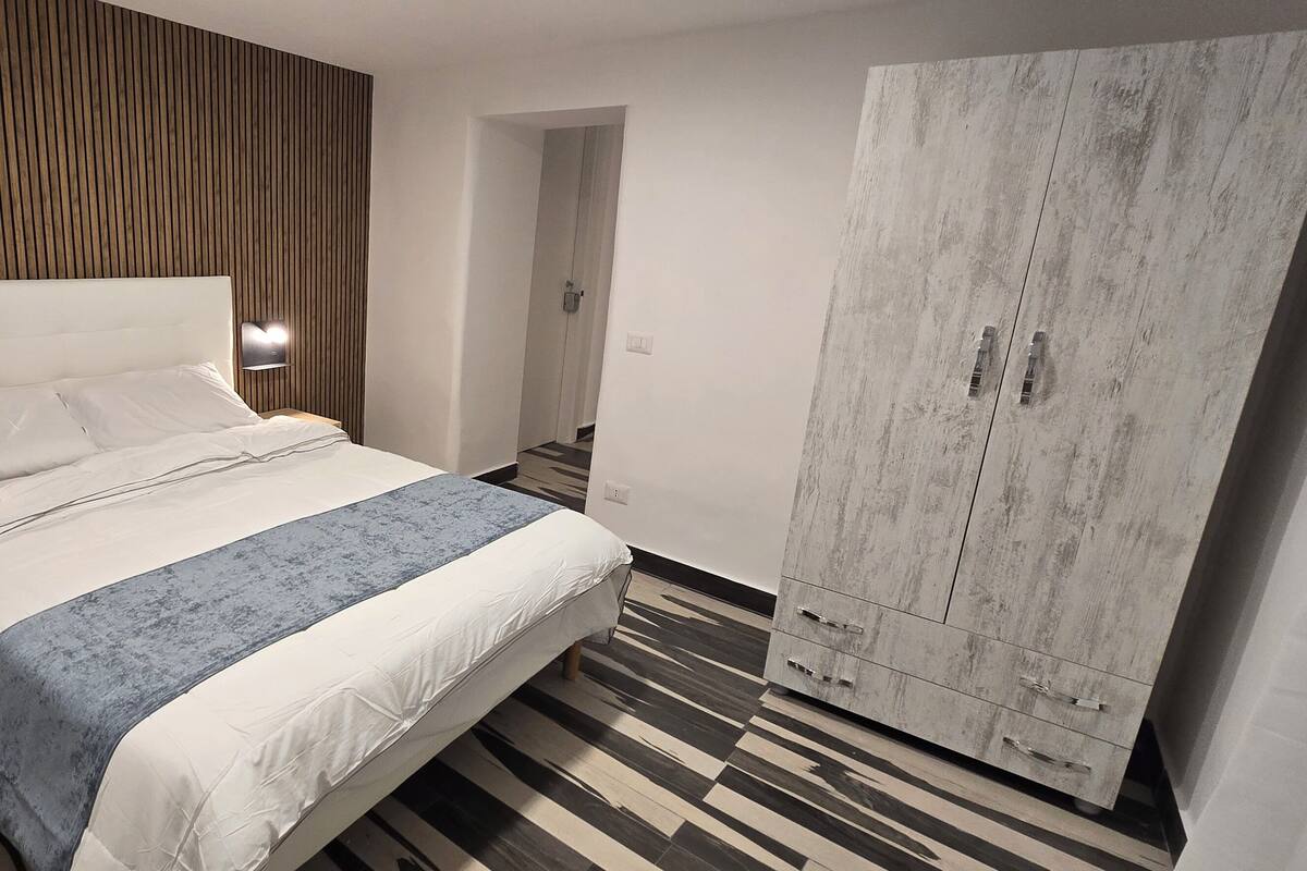 A hotel room with a bed, bedside tables, a wardrobe, and a wooden wall panel.