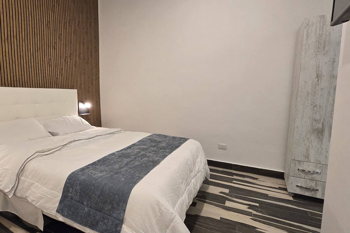 A modern bedroom with a large bed, bedside tables, a TV, and a wardrobe.