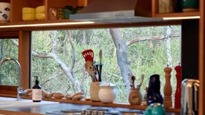 Een keuken met houten planken, een raam met uitzicht op bomen en diverse keukengerei op het aanrecht.