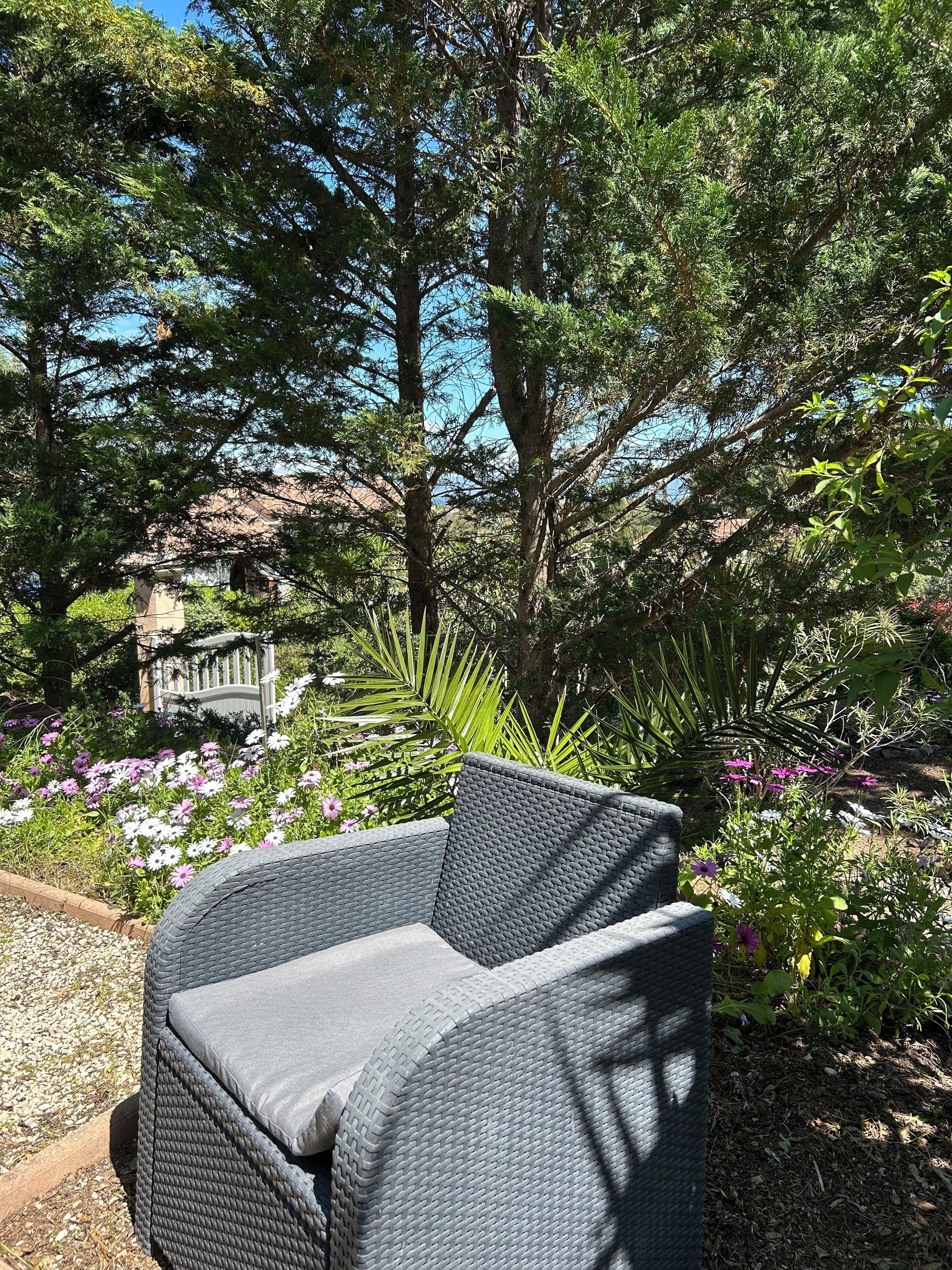 A wicker chair in a garden with various plants and a stone bench.