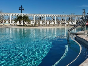 Une piscine aux eaux cristallines, avec une pergola blanche et des chaises longues à l’arrière-plan.