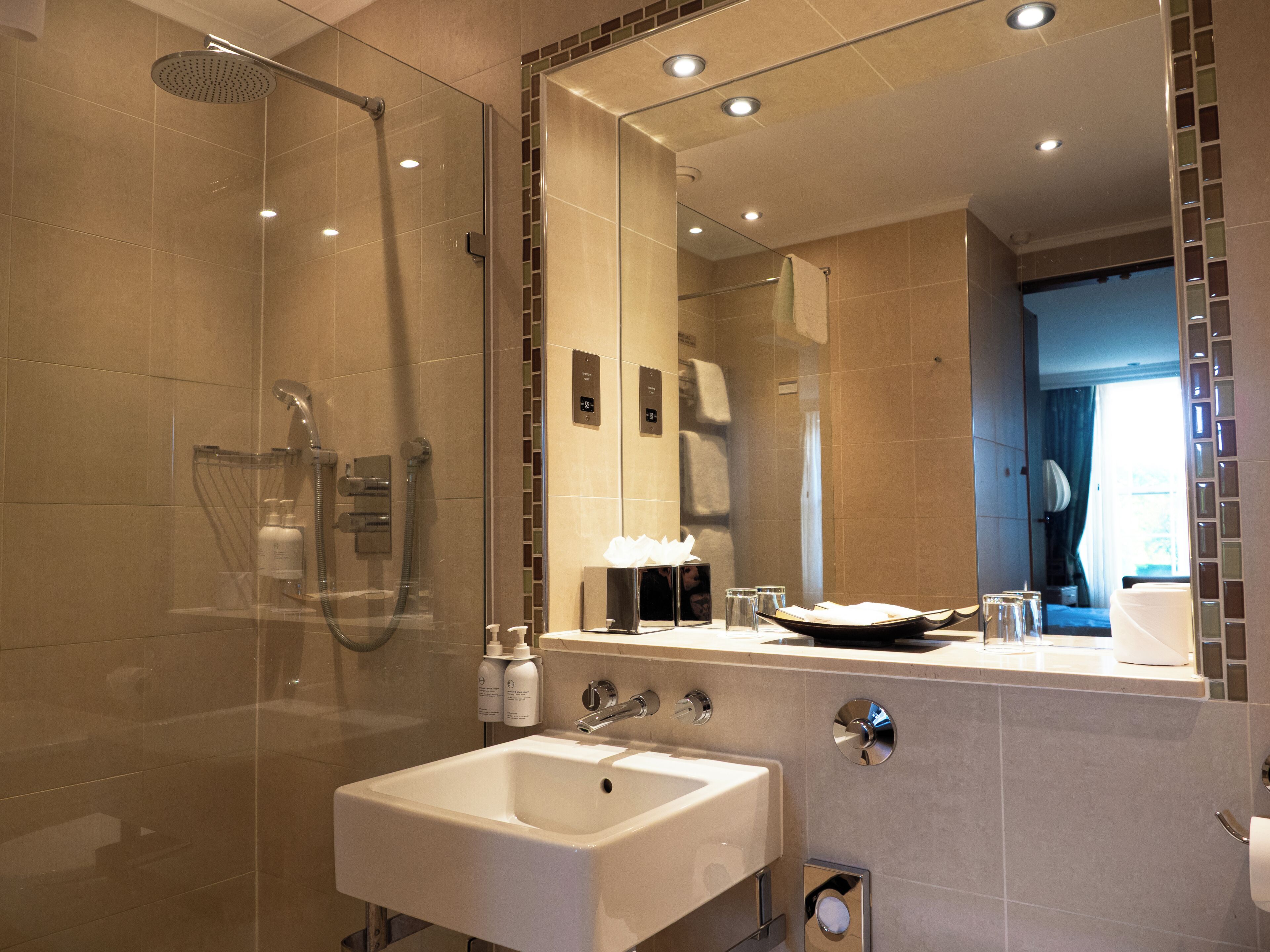 A modern bathroom with a glass-enclosed shower, a white sink, and a large mirror reflecting the room.