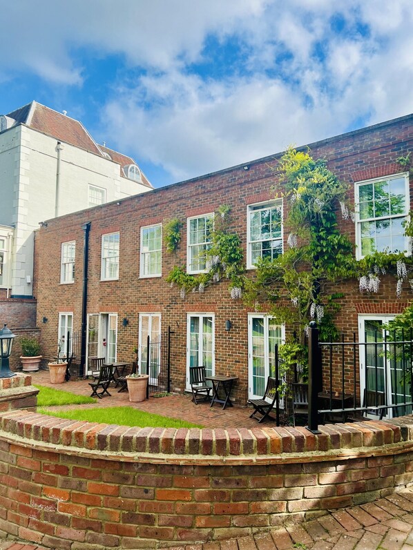 A brick building with white-framed windows, a small garden area with tables and chairs, and a brick wall surrounding the space. - St Michael's Manor Hotel (St Albans)