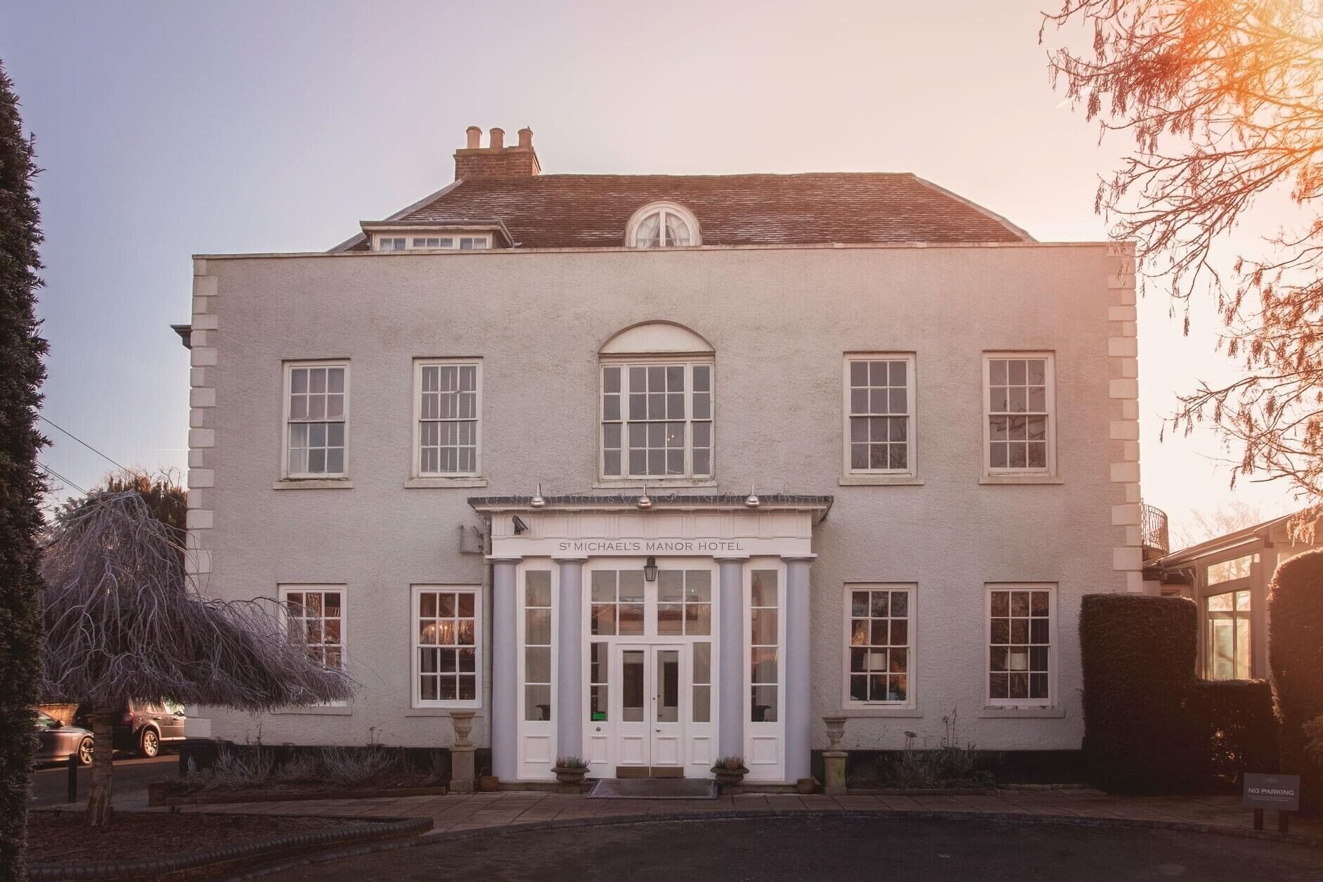 A two-story building with a central entrance, large windows, and a sign reading 'St Michael's Manor Hotel'.