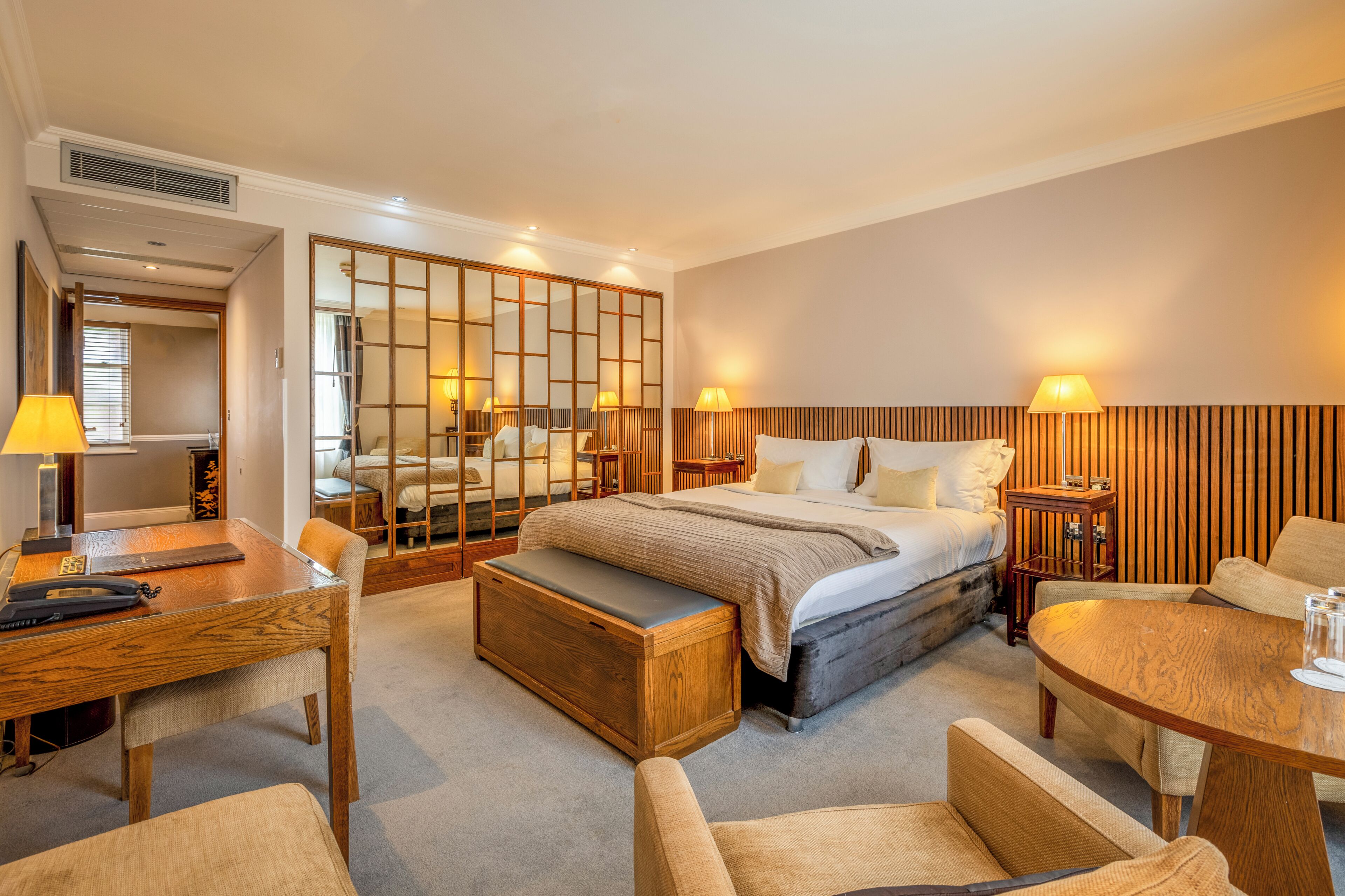 A hotel room with a bed, bedside tables, a desk, and a seating area.