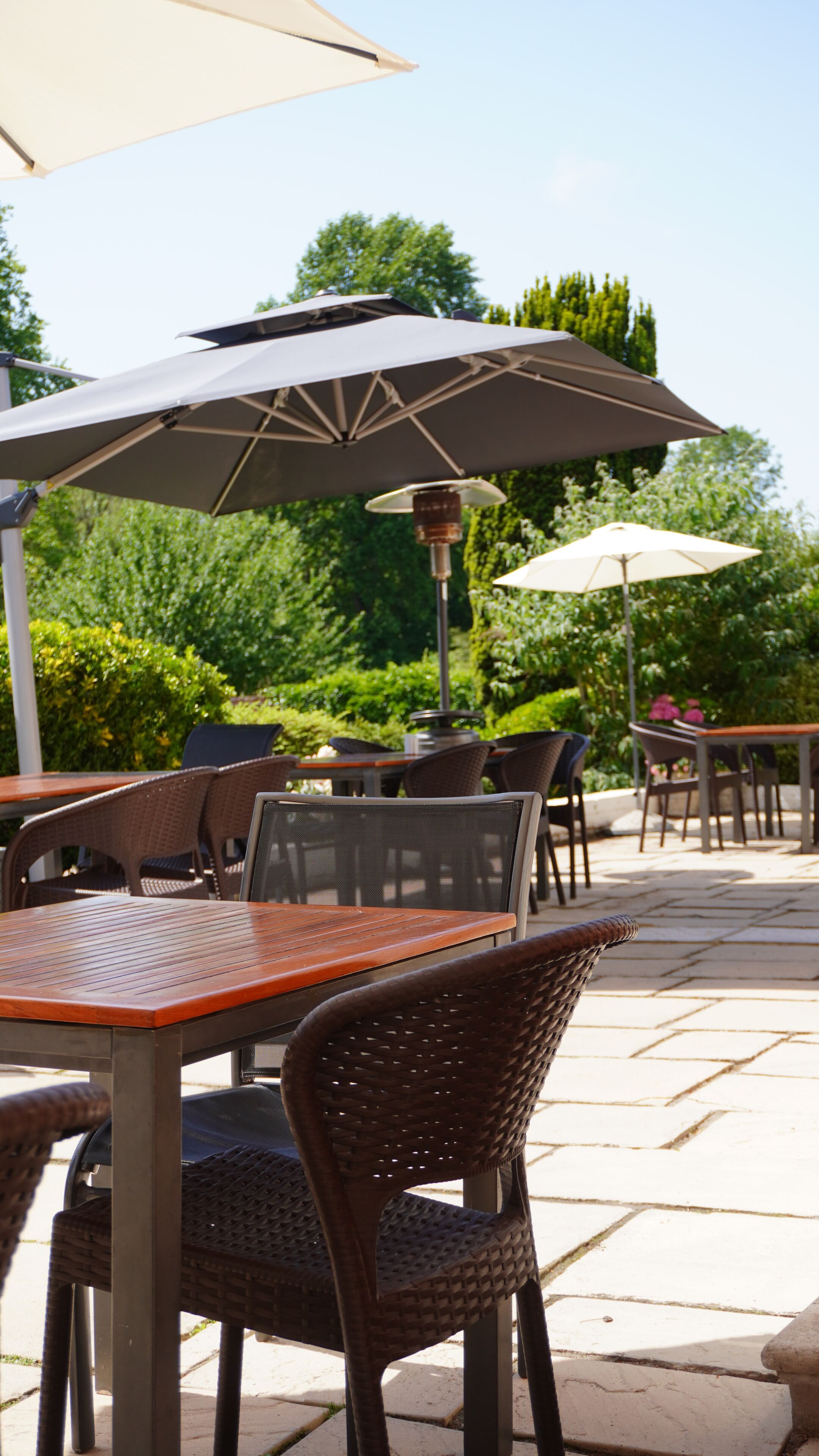 An outdoor patio with tables and chairs, a large umbrella, and a lamp post.