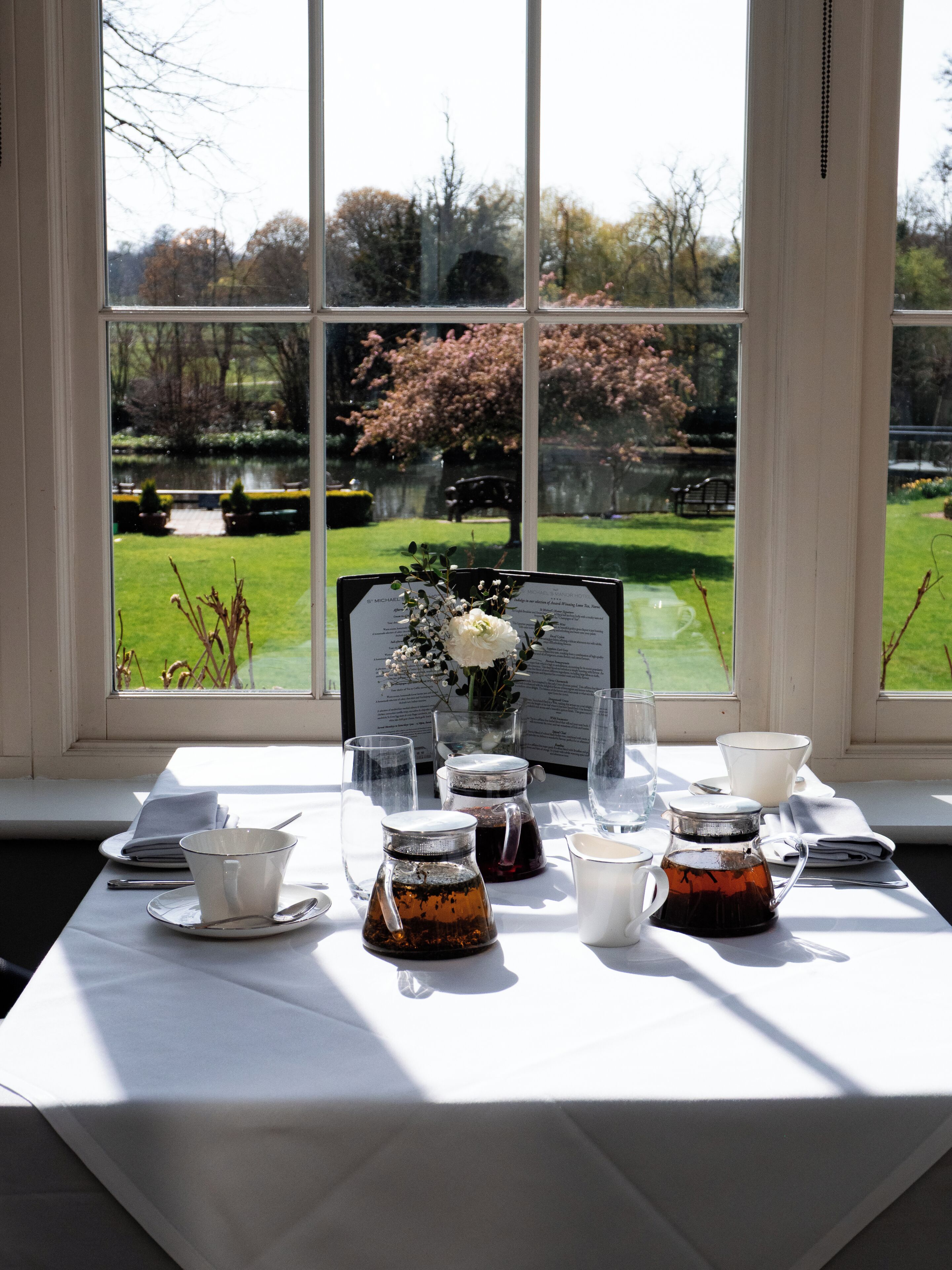 A table set for tea with a view of a garden through large windows.