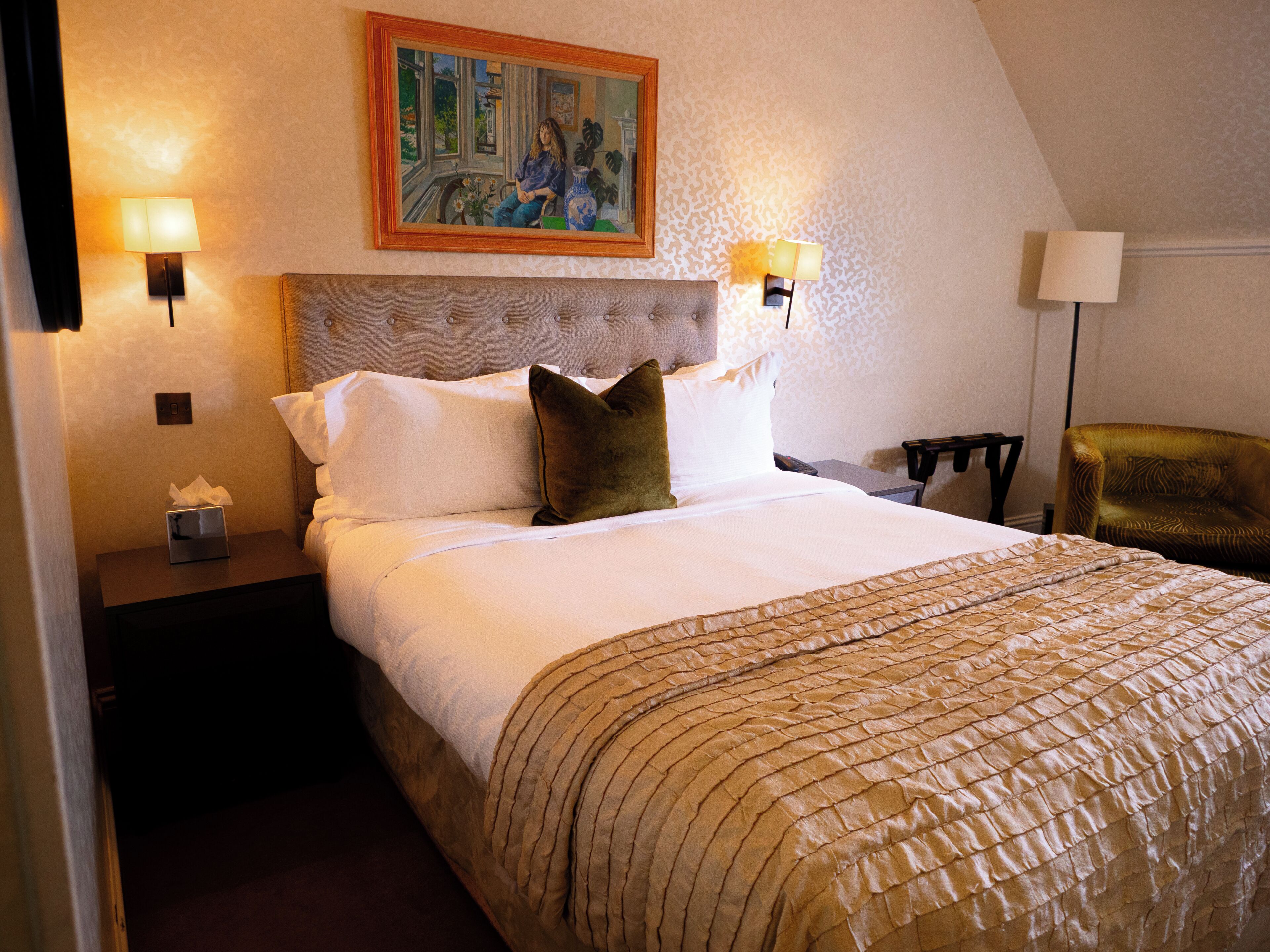 Une chambre d’hôtel avec un lit, un tableau au mur, deux lampes de chevet, une table de chevet avec une boîte de mouchoirs et une chaise.