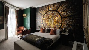 A spacious bedroom with a large bed, a round stained glass window, a small table, and a chair. - St Michael's Manor Hotel (St Albans)