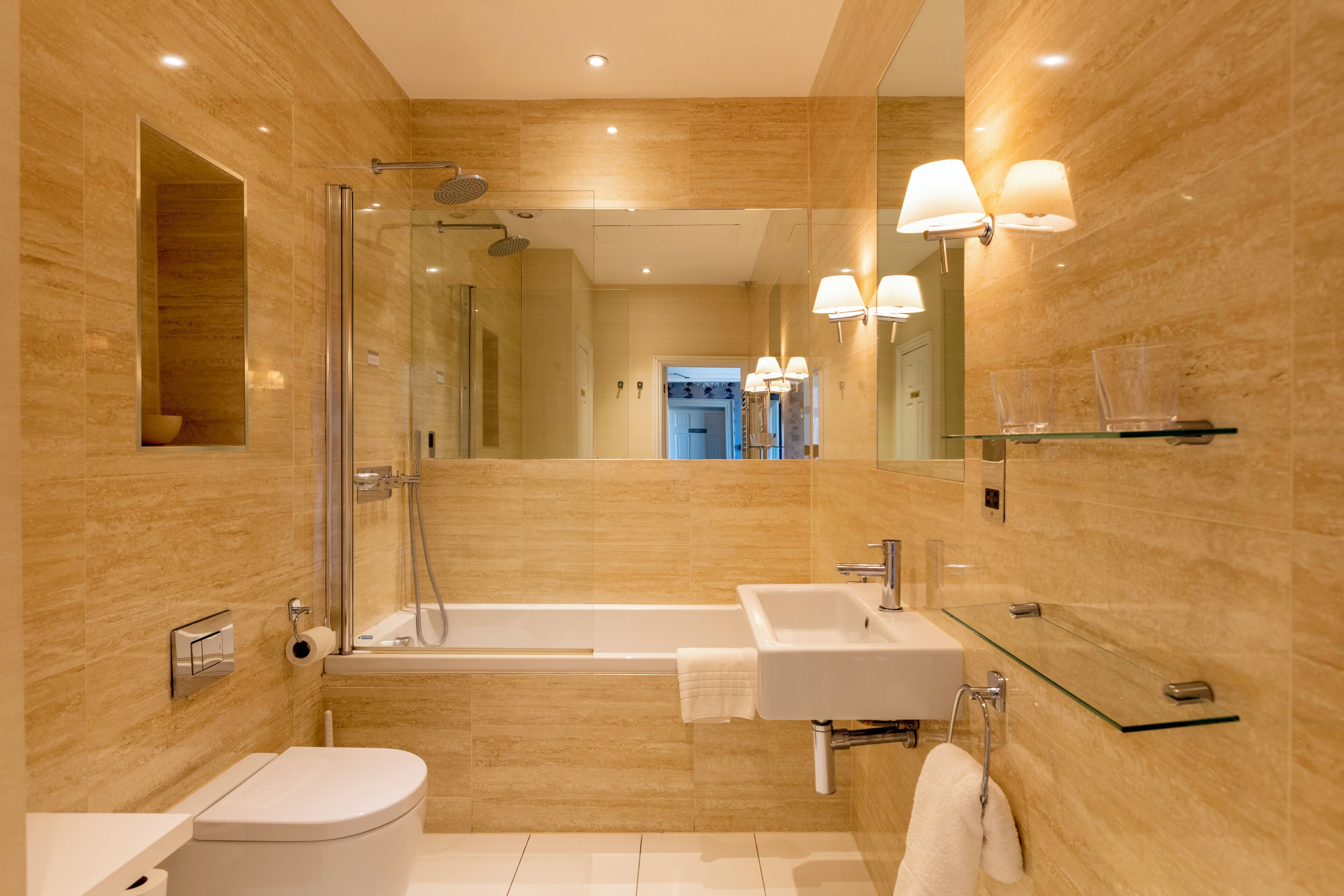 A modern bathroom with a glass shower enclosure, a standalone toilet, a freestanding bathtub, and a glass-topped vanity with a mirror.