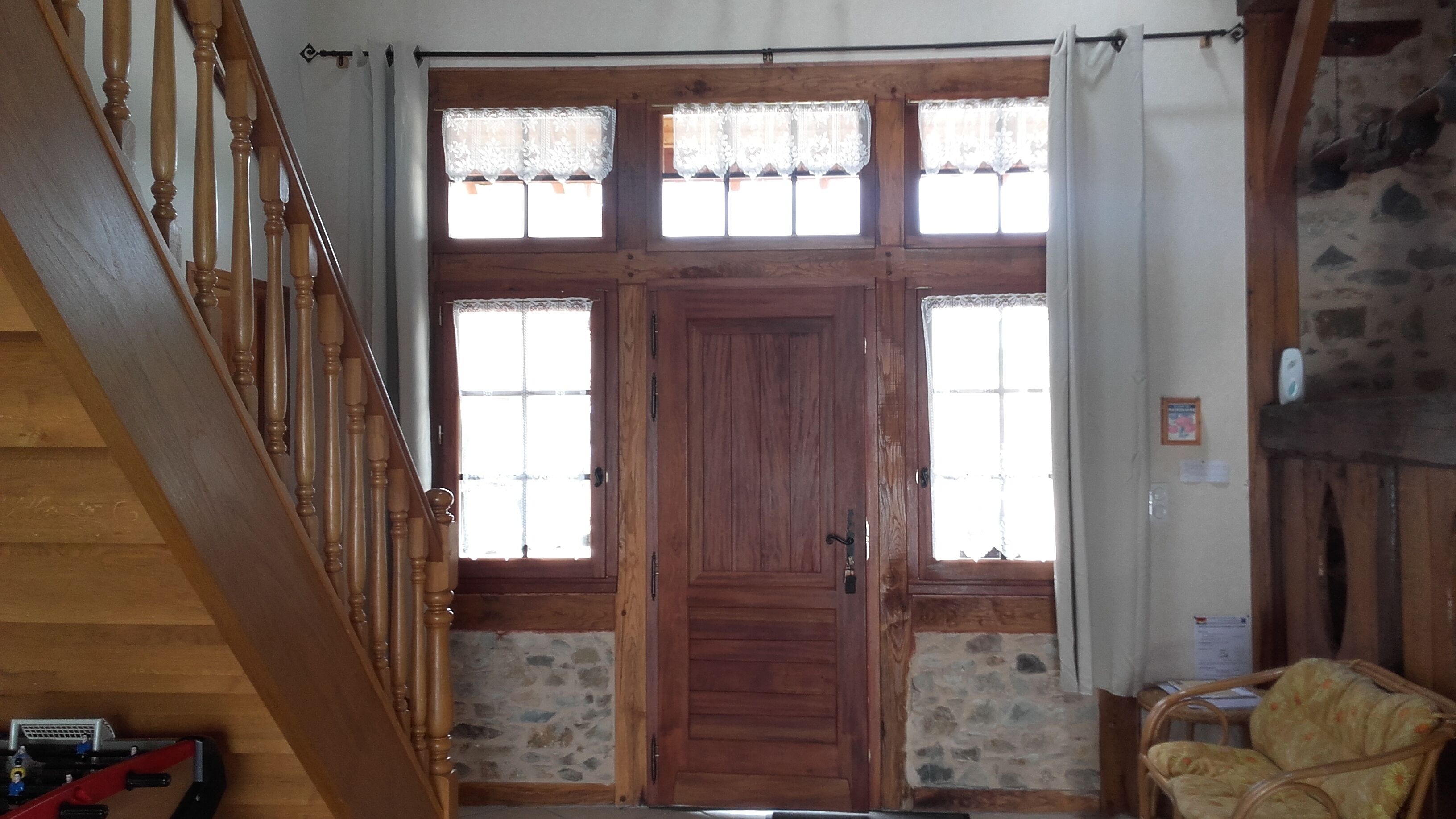 Un escalier en bois avec une rampe, une grande porte en bois dotée de panneaux de verre et un mur en pierre.